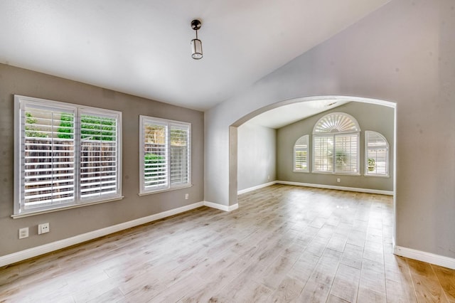 empty room featuring lofted ceiling, wood finished floors, arched walkways, and baseboards