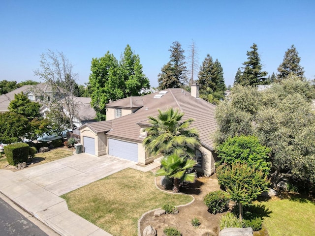 view of front of house featuring a tiled roof, an attached garage, concrete driveway, and a front yard