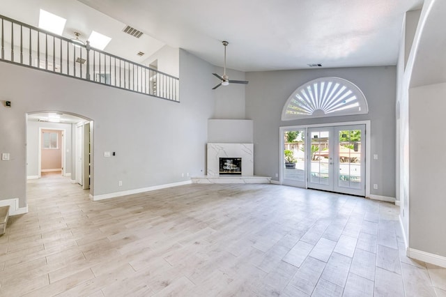 unfurnished living room with ceiling fan, high vaulted ceiling, arched walkways, baseboards, and wood finished floors