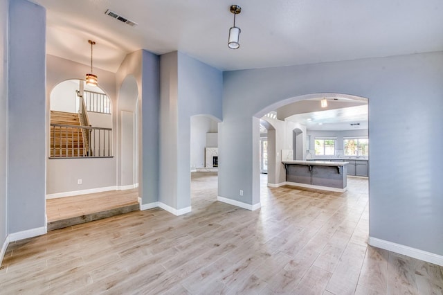 unfurnished living room featuring arched walkways, light wood-type flooring, and baseboards