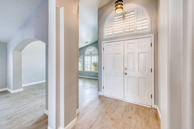 foyer featuring light wood-style floors, baseboards, arched walkways, and lofted ceiling