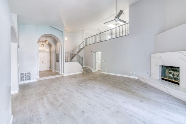 unfurnished living room with arched walkways, a ceiling fan, wood finished floors, high vaulted ceiling, and stairway