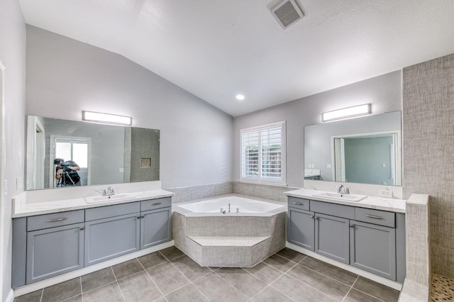 full bath with vaulted ceiling, a garden tub, two vanities, and tile patterned flooring