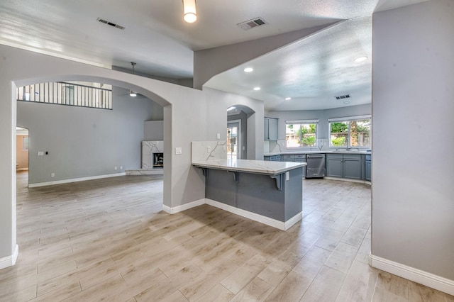 kitchen with dishwasher, light wood-style floors, a breakfast bar, arched walkways, and recessed lighting