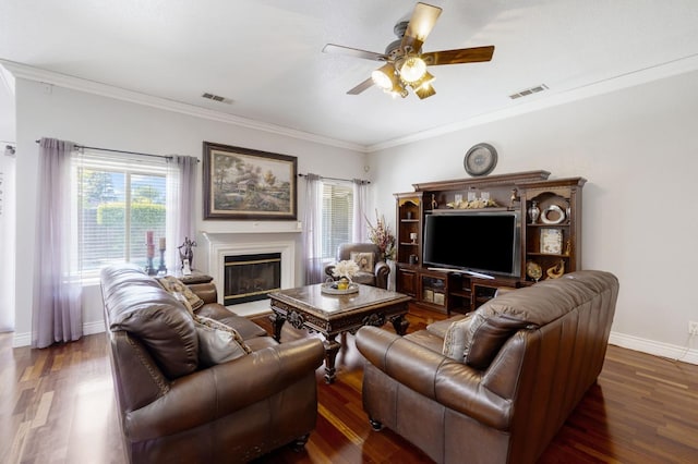 living area with a ceiling fan, wood finished floors, crown molding, a glass covered fireplace, and baseboards