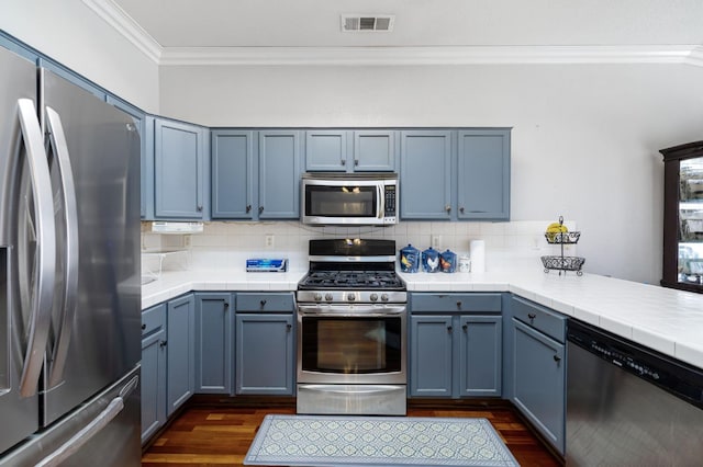 kitchen with stainless steel appliances, ornamental molding, dark wood-style flooring, decorative backsplash, and a peninsula