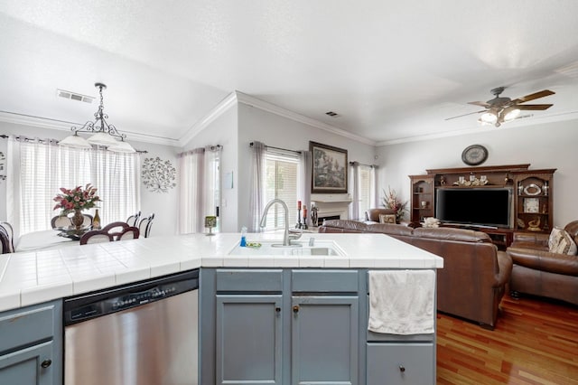 kitchen featuring stainless steel dishwasher, a sink, open floor plan, crown molding, and light wood-style floors