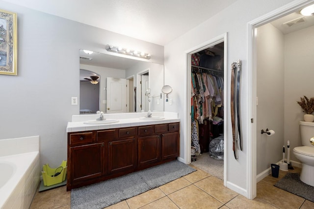 bathroom featuring toilet, double vanity, tile patterned flooring, a bath, and a walk in closet