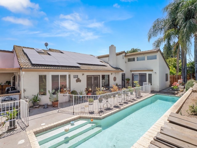 rear view of house featuring stucco siding, french doors, a tiled roof, a patio area, and roof mounted solar panels