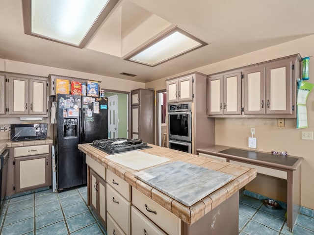 kitchen with black appliances, tile counters, tile patterned flooring, and a center island