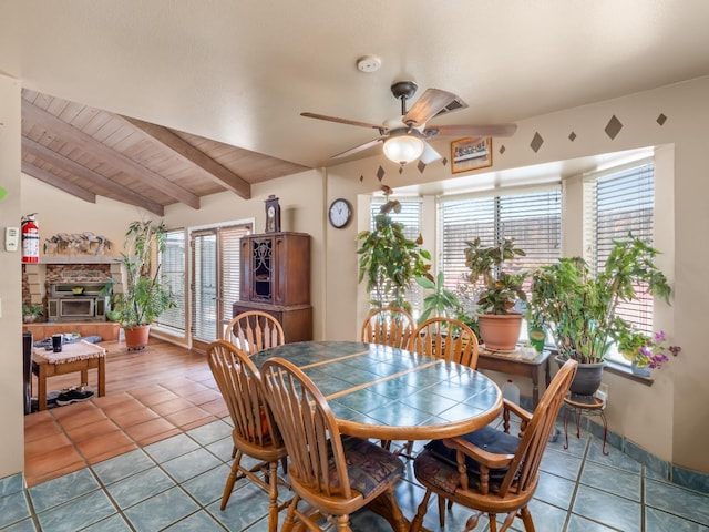 dining area featuring ceiling fan, tile patterned floors, a stone fireplace, and wooden ceiling