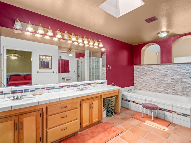 bathroom with a ceiling fan, a skylight, tile patterned flooring, a shower stall, and double vanity