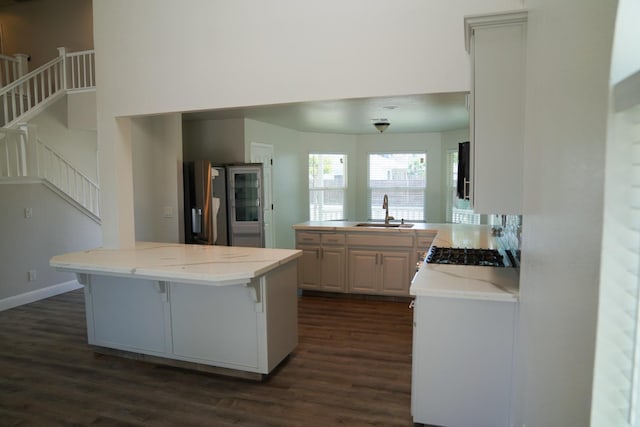 kitchen with a sink, dark wood-type flooring, a center island, a breakfast bar, and light stone counters