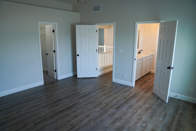 unfurnished bedroom with baseboards, dark wood-style floors, a sink, a walk in closet, and a high ceiling