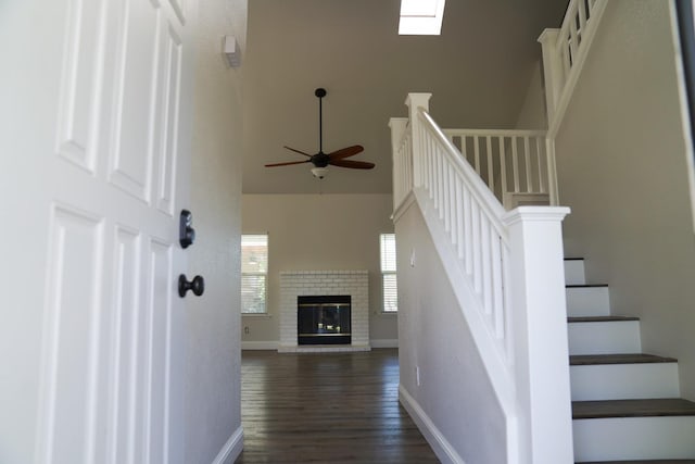 staircase with a towering ceiling, a ceiling fan, wood finished floors, baseboards, and a fireplace