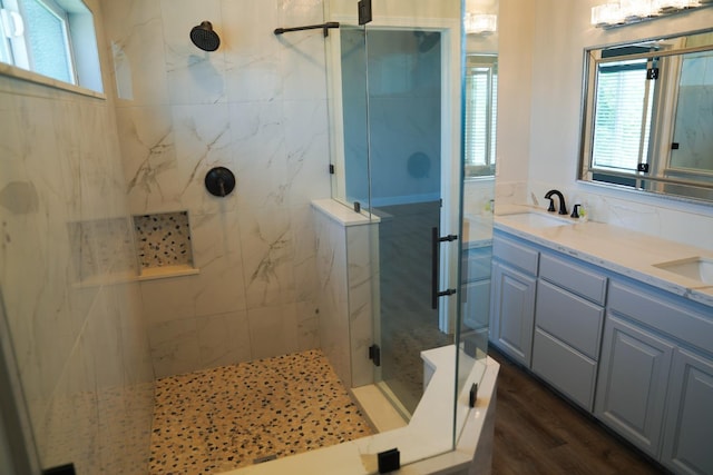 bathroom with a marble finish shower, healthy amount of natural light, double vanity, and wood finished floors