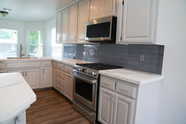 kitchen with appliances with stainless steel finishes, a sink, decorative backsplash, and light stone countertops