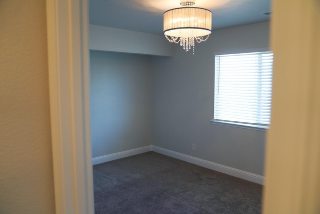 spare room with dark carpet, a chandelier, and baseboards