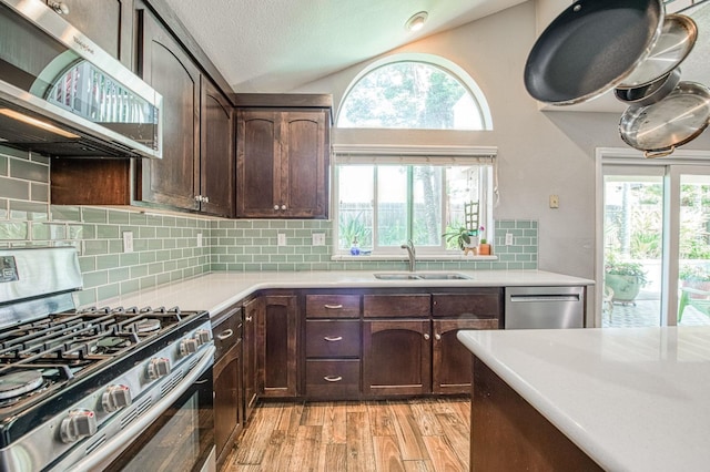 kitchen featuring stainless steel appliances, a sink, vaulted ceiling, light countertops, and light wood finished floors