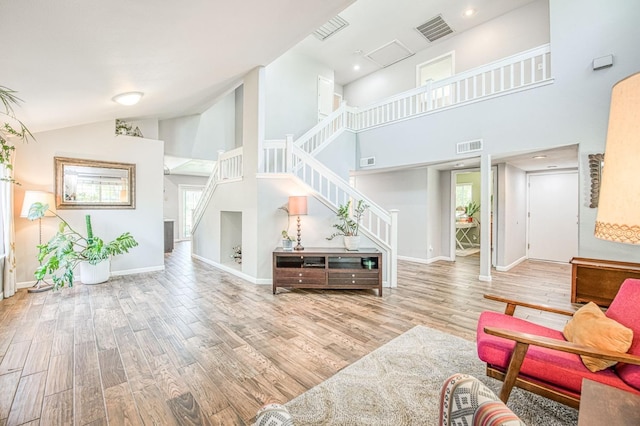 living room featuring high vaulted ceiling, wood finished floors, stairway, and baseboards