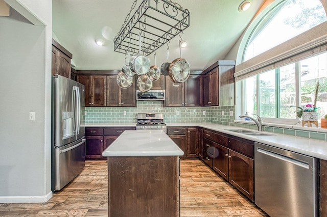 kitchen with stainless steel appliances, a sink, a center island, light countertops, and light wood finished floors