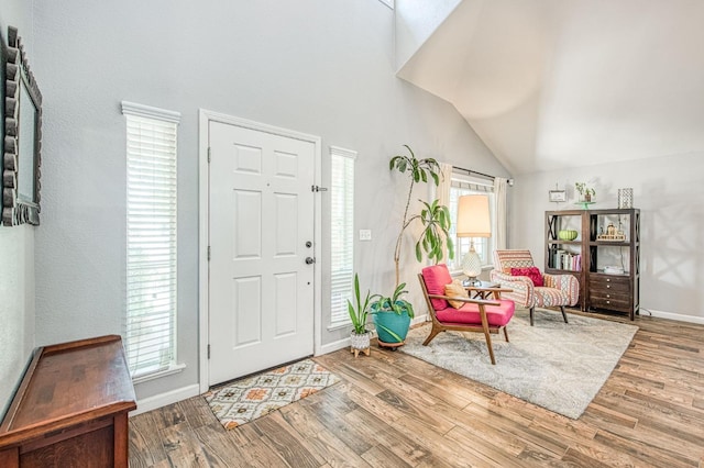 entryway with wood finished floors, baseboards, and high vaulted ceiling