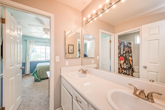 ensuite bathroom with toilet, double vanity, a ceiling fan, and baseboards