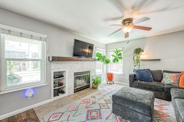 living area featuring healthy amount of natural light, baseboards, ceiling fan, and a fireplace with flush hearth