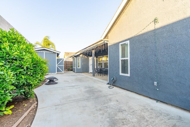 view of patio featuring a storage unit, an outbuilding, fence, and outdoor dining space