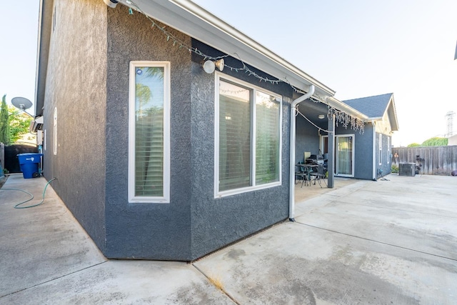 view of side of home featuring stucco siding, a patio, fence, and central air condition unit