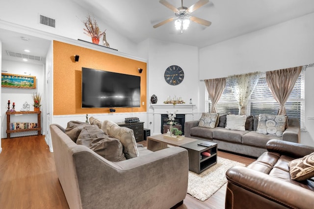 living area with wood finished floors, ceiling fan, a fireplace, and a wainscoted wall