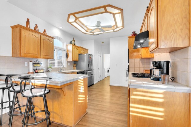 kitchen featuring a peninsula, tile counters, stainless steel refrigerator with ice dispenser, a breakfast bar area, and ceiling fan
