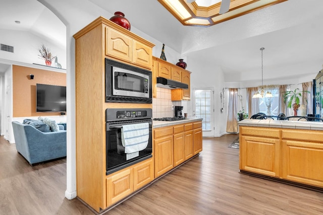 kitchen with black appliances, light wood-style floors, under cabinet range hood, tile counters, and open floor plan