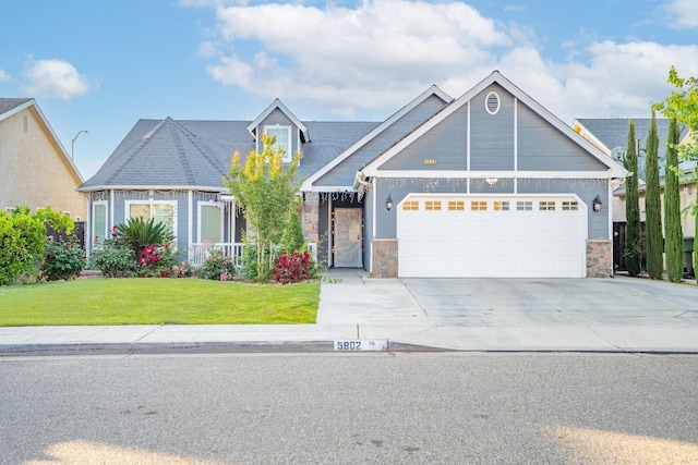view of front of home featuring a front lawn, stone siding, a garage, and concrete driveway