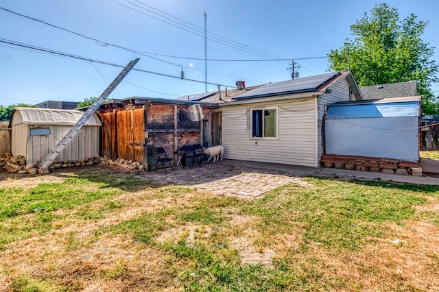 back of property featuring a storage unit, roof mounted solar panels, a patio, and an outbuilding