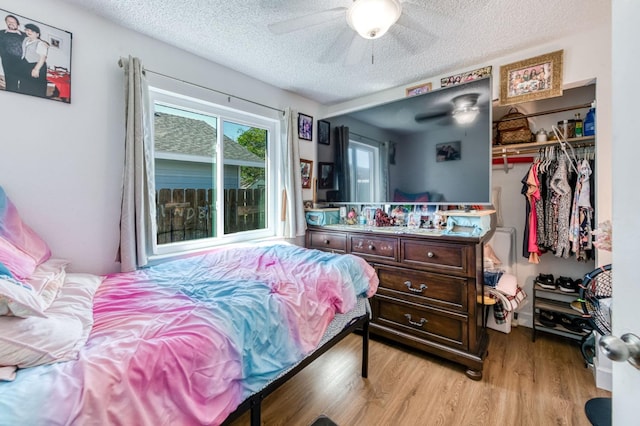 bedroom featuring light wood-type flooring, a textured ceiling, a closet, a ceiling fan, and a spacious closet
