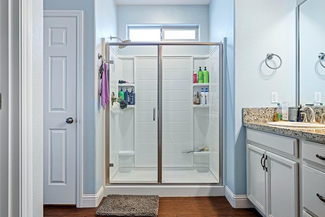 bathroom with a stall shower, wood finished floors, vanity, and baseboards