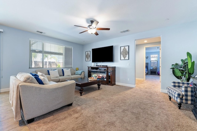 living room featuring a ceiling fan, plenty of natural light, baseboards, and light colored carpet