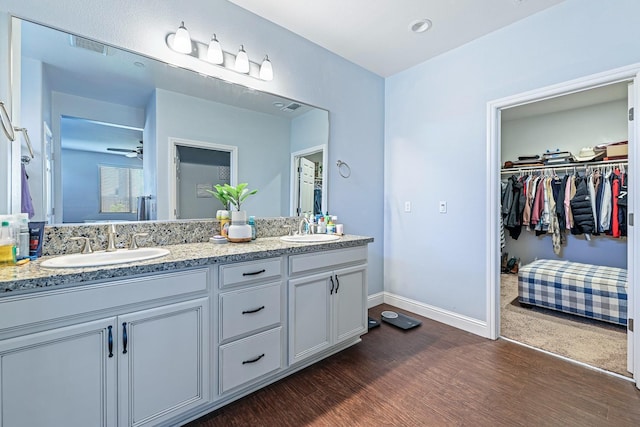 bathroom featuring wood finished floors, double vanity, a spacious closet, and baseboards