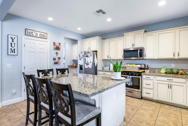 kitchen featuring appliances with stainless steel finishes, light tile patterned floors, a breakfast bar, light stone counters, and recessed lighting
