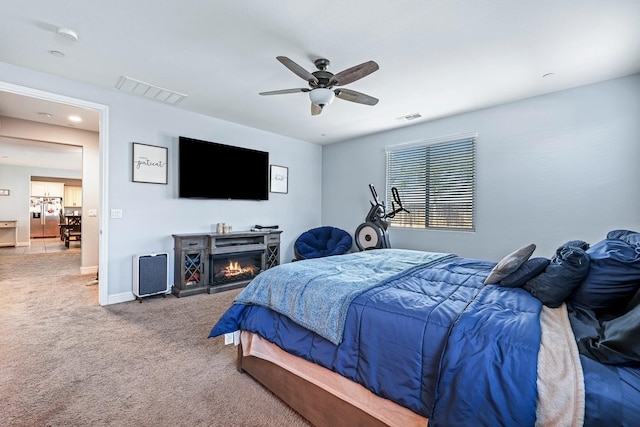 bedroom featuring stainless steel refrigerator with ice dispenser, carpet floors, a ceiling fan, baseboards, and a lit fireplace