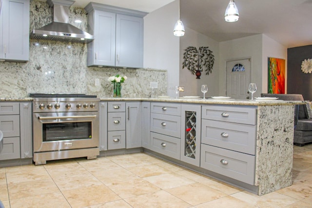 kitchen with high end range, gray cabinets, wall chimney range hood, a peninsula, and backsplash