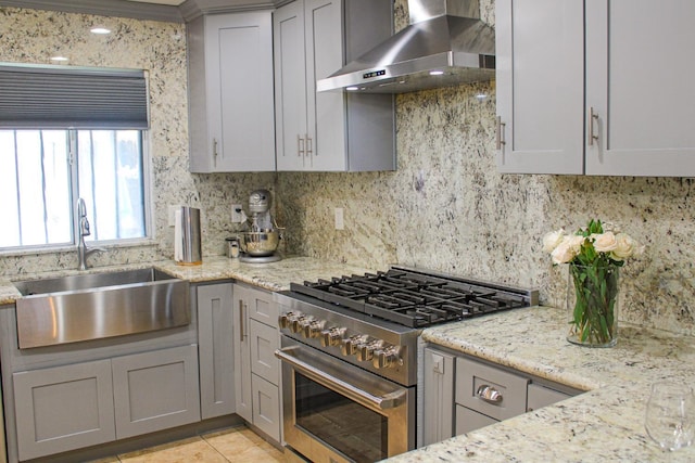 kitchen with high end stainless steel range oven, wall chimney range hood, a sink, and gray cabinetry
