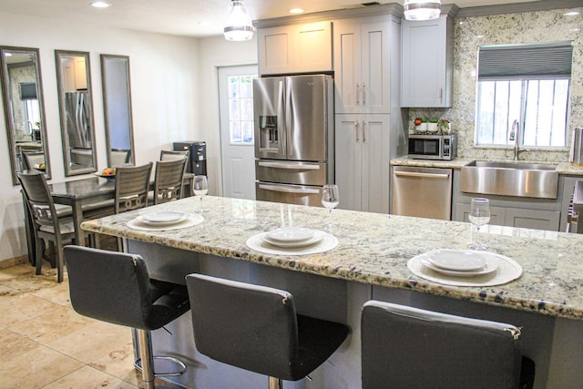 kitchen featuring stainless steel appliances, a sink, a kitchen breakfast bar, light tile patterned floors, and light stone countertops