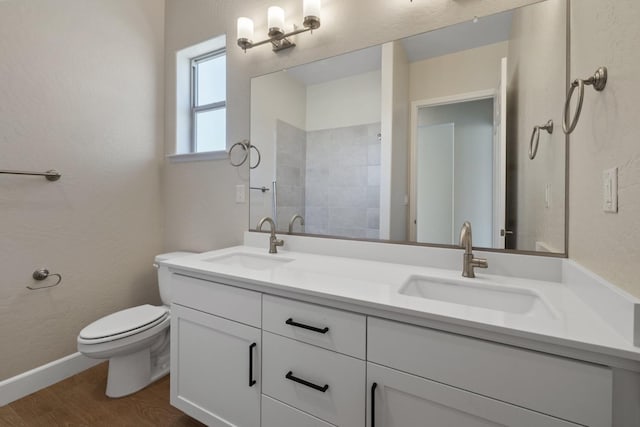bathroom featuring toilet, wood finished floors, double vanity, baseboards, and a textured wall