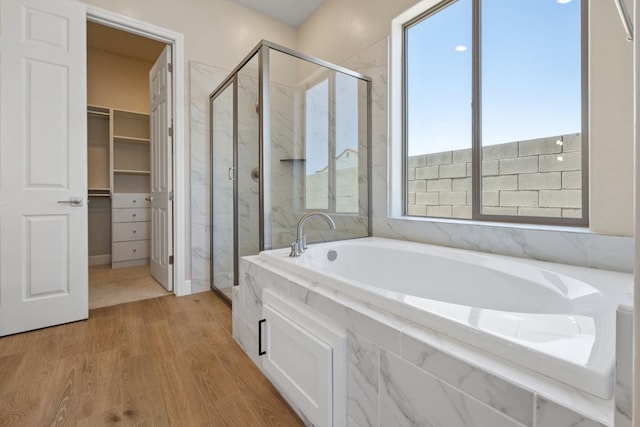 full bathroom featuring wood finished floors, a stall shower, a garden tub, and a spacious closet