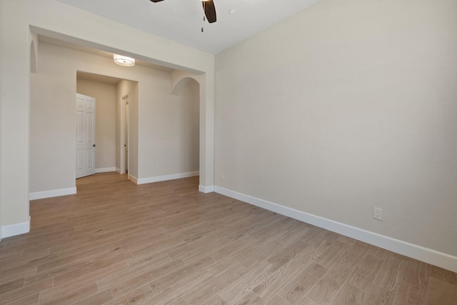 unfurnished room with ceiling fan, light wood finished floors, baseboards, arched walkways, and a smoke detector