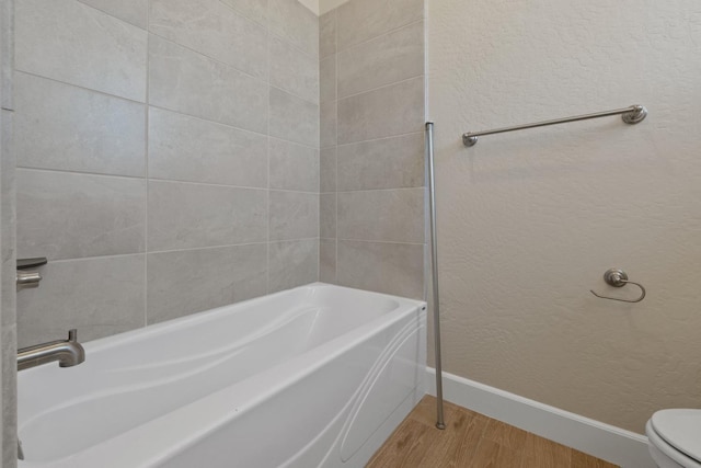 bathroom with wood finished floors, a tub to relax in, baseboards, toilet, and a textured wall
