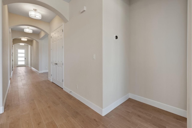 hall with baseboards, light wood-style floors, and arched walkways