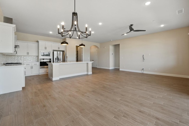 kitchen with appliances with stainless steel finishes, open floor plan, arched walkways, decorative backsplash, and light wood finished floors